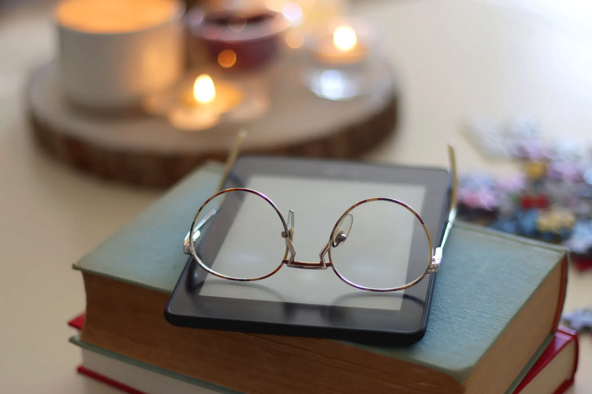 A pair of eyeglasses resting on a stack of books with a warm candlelit background.