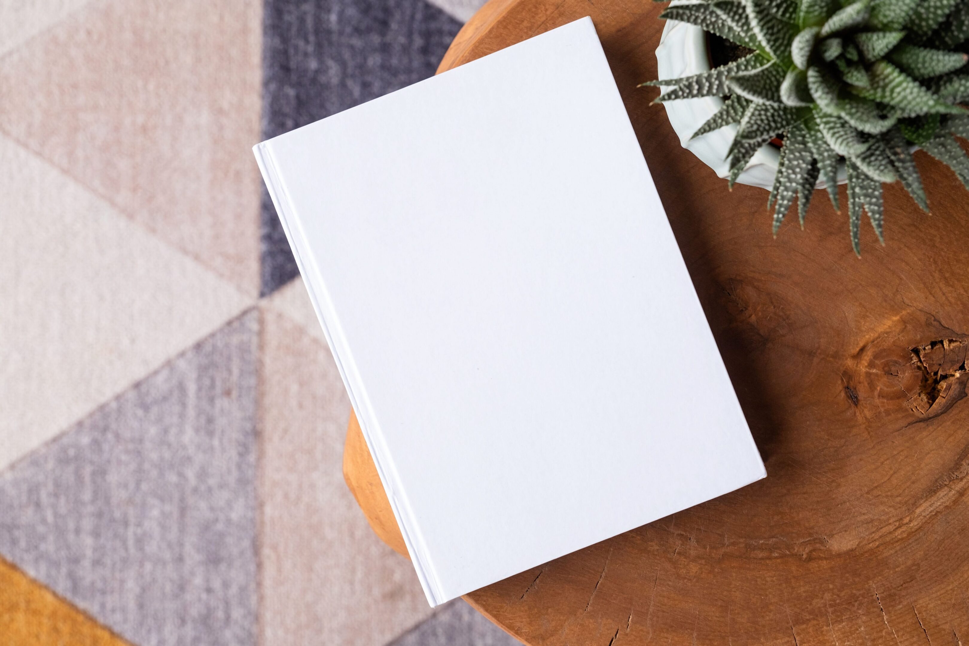 Blank white book on a wooden table next to a plant.